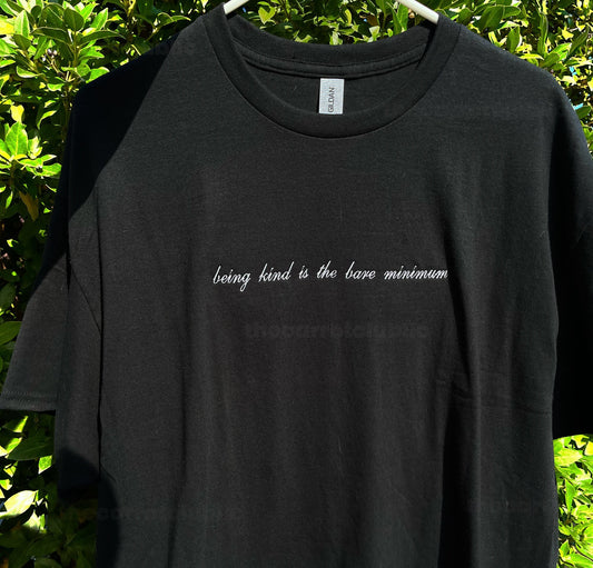 Black Crewneck T-shirt with White embroidery lettering in a script font with the words &quot;being kind is the bare minimum&quot; Minimalistic white small embroidery on the front chest.